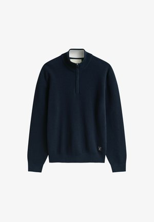 Marineblauwe gebreide trui met lange mouwen, geribde kraag, halve ritssluiting aan de voorkant en een klein merkembleem bij de zoom.