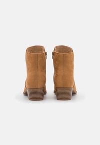 Beżowe zamszowe botki za kostkę z bocznym zamkiem, krótkim obcasem typu stacked i gładką fakturą. Obcas ozdobiony jest paskowanym akcentem.