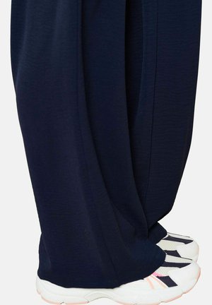 Navy wide-leg pants with a textured finish, paired with white sneakers featuring navy and pink accents, showing a layered, relaxed fit.