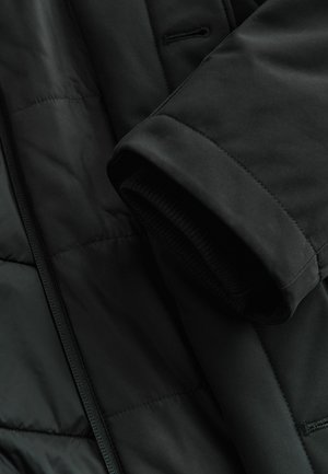 Musthave musta isoleeritud jakk siledast materjalist, ribatud mansettide ja elegantse kujundusega. Omab tikitud tekstuuri ja varjatud taskuid.