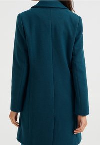 Teal ullblandad kappa med en lång, skräddarsydd design, snedskuren krage och en mjuk textur med en strömlinjeformad silhuett.