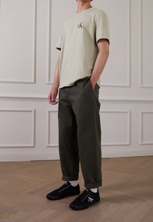 Ljusgrön bomulls t-shirt med CK-logotyp, olivgröna byxor och svarta sneakers med vita detaljer och snören. Avslappnad och ledig passform.