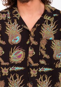 Chemise noire à manches courtes avec un imprimé coloré sur le thème sous-marin, présentant des motifs détaillés de créatures marines en violet et turquoise, et une poche poitrine.