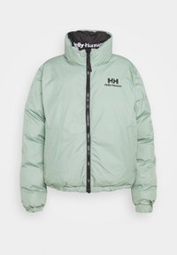 Veste matelassée verte menthe avec col haut, fermeture éclair noire, et logo Helly Hansen sur la poitrine. Tissu texturé et poignets élastiques.