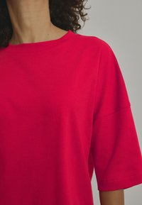 T-shirt rosso brillante a maniche corte con scollatura a girocollo. Tessuto morbido e vestibilità leggermente ampia, che termina a metà bicipite. Design semplice senza fantasie.