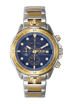 Montre à cadran bleu avec accents dorés, bracelet en acier inoxydable et en ton or, sous-cadrans et détail de tête de lion sur le côté. Fonction chronographe visible.