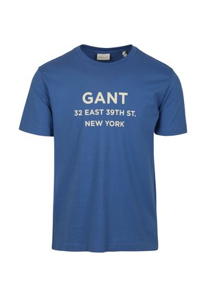 Blauw katoenen T-shirt met witte tekst: "GANT 32 EAST 39TH ST. NEW YORK." Korte mouwen en ronde halslijn, gladde textuur.