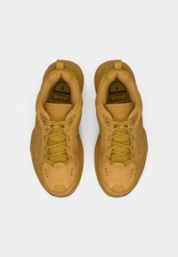 Een paar tan Nike Air Monarch sneakers met veters, gezien van bovenaf op een witte achtergrond.