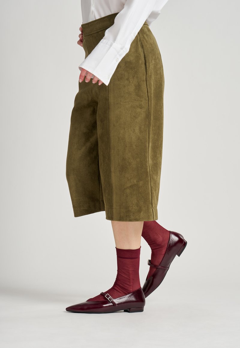 Olijfgroene sued culottes met een wijde pijpdesign. Gecombineerd met kastanjebruine doorzichtige sokken en bordeaux patent leren flatschoenen met gespen.