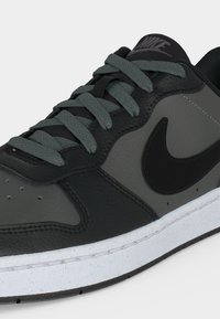Μαύρο και σκούρο γκρι παπούτσι Nike με σκούρα γκρι κορδόνια και λευκή σόλα, που δείχνει λεπτομέρειες από την πλευρά και την κορυφή σε λευκό φόντο.