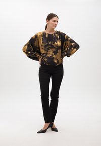 Maglietta oversize a maniche lunghe nera e dorata con motivo tie-dye, colletto rotondo, abbinata a pantaloni neri attillati e décolleté neri a punta.