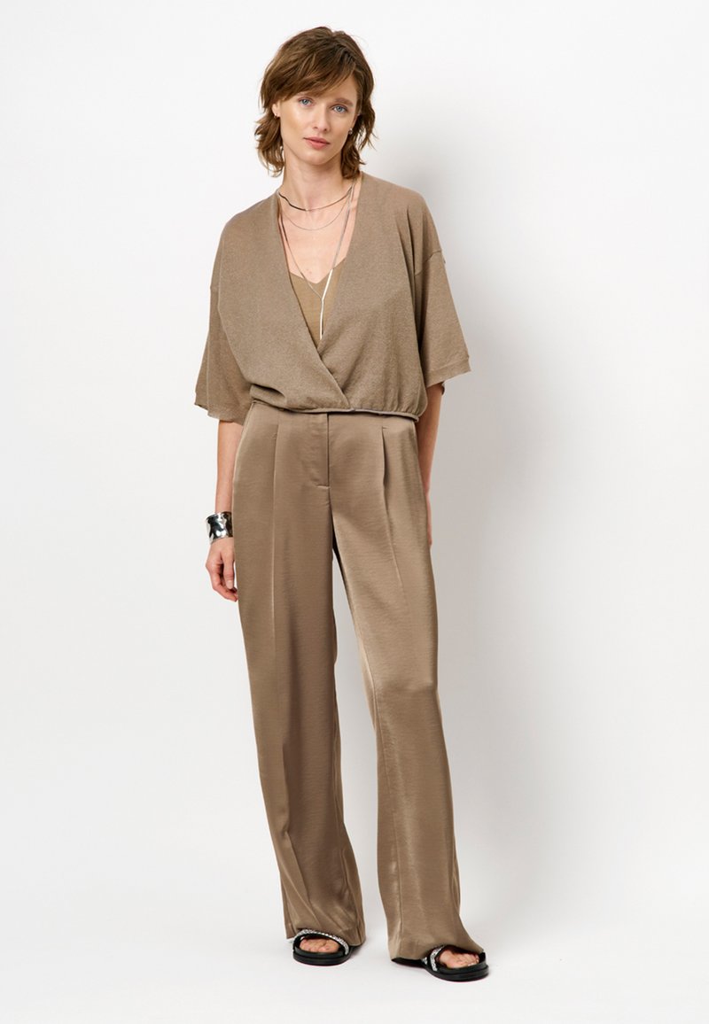 Taupe, korte mouwen wikkelshirt gecombineerd met hoge taille, brede broekspijpen. Glad textuur, minimalistisch ontwerp en laagjes van subtiele accessoires.