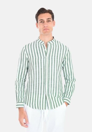 Uomo che indossa una camicia a maniche lunghe a righe verticali verdi e bianche con collo alla coreana e pantaloni bianchi su sfondo uniforme.