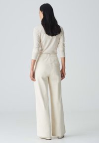 Crème kleurige ribben brede broek met een hoge tailleband en achterzak, gecombineerd met een lichtbeige lange mouw top.