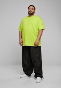 T-shirt sovradimensionato a maniche corte di colore verde neon con scollo rotondo, abbinato a pantaloni larghi scuri e sneakers bianche.