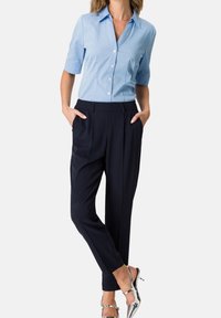 Hellblaues kurzärmeliges Hemd mit Knöpfen, dunkelblaue, maßgeschneiderte Hose mit Seitentaschen und silberne, Riemchen-High-Heel-Schuhe. Klassisches Design.