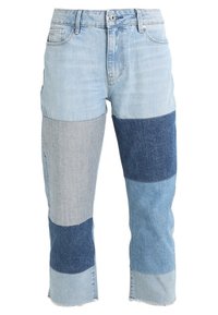 Ljust blå patchwork-jeans med skiftande nyanser av denim. Påtagliga detaljer inkluderar olika texturer och en rå kant vid muddar.