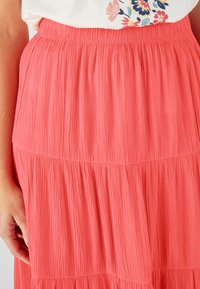 Jupe tiered corail avec texture froissée, taille élastique, design mi-long, mettant en valeur un tissu doux et léger.