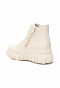 Zapatillas altas en cuero beige claro. Cuentan con una suela texturizada y estriada, y un zipper lateral para facilitar el uso. Diseño minimalista.