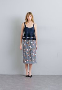 Ναυτικό τοπ με πεπλώγια λεπτά λουριά, σε συνδυασμό με γκρί φλοράλ φούστα με κόκκινες και πράσινες λεπτομέρειες, φορεμένο με μαύρες γόβες.