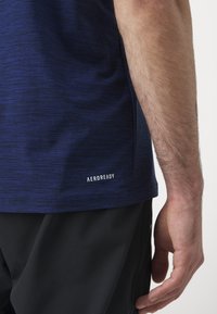 Navy blue short-sleeve shirt with a textured pattern. Features "AEROREADY" branding near the hem. Worn with black athletic shorts.
