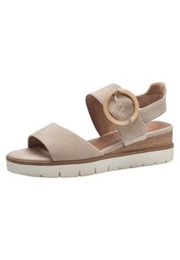 Sandale en suède beige avec une large bride avant, une bride au niveau de la cheville réglable avec un anneau en métal doré, et une semelle plateforme blanche avec un détail en bois.
