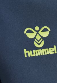 Marinblått textil med en framträdande gul Hummel-logotyp, stiliserad bikunskap och fet text längst ner.