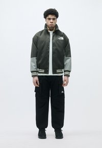 Olíva zöld bombázó dzseki szürke ujjakkal, patent gombokkal és logó részlettel. Fekete cargo nadrág és fekete cipők teszik teljessé a szettet.