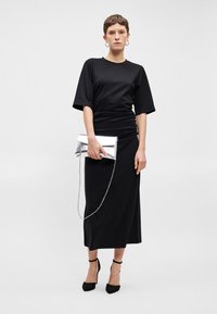 Μαύρο φορεματάκι t-shirt με κοντά μανίκια, συγκεντρωμένη λεπτομέρεια στη μέση, συνδυασμένο με ασημένια μεταλλική τσάντα και μαύρες γόβες με λουράκι γύρω από τον αστράγαλο.