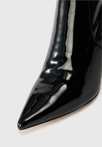 Chaussure à talon haut en cuir verni noir avec un bout pointu et une texture lisse et brillante. Présente une silhouette élégante et élancée.