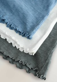 Pile de trois pièces de tissu tricoté léger en bleu, blanc et gris, chacune avec un détail de bord à volants roulés.