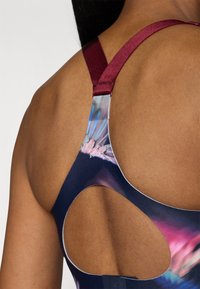 Sportsbh med et mørkeblått og lilla mønster, med et utskjæringsdesign på ryggen og justerbare bånd i bordeaux for en sikker passform.