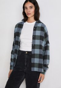 Flanellen overhemd in een blauw en zwart ruitpatroon, met een knoopsluiting aan de voorkant, een gespreidde kraag en een ontspannen pasvorm, gecombineerd met hoge zwarte broeken.