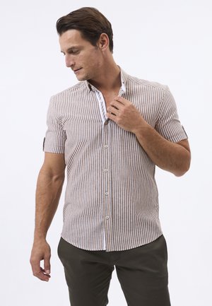 Camicia a maniche corte a righe marroni e bianche con colletto strutturato, apertura con bottoni, tessuto testurizzato e dettaglio del primo bottone. Indossata con pantaloni scuri.