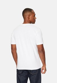  camiseta de algodón blanca de manga corta, con cuello redondo y una textura suave; combinada con jeans de mezclilla azul oscuro.