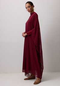Bordo haljina do poda s visokim v-neck izrezom i lepršavim rukavima, napravljena od lagane tkanine. Ima prozirne panele i opušteni kroj.