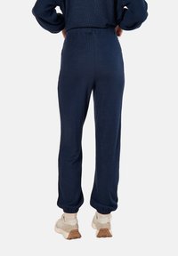 Marineblau Jogginghosen mit strukturierter Oberfläche, elastischem Bund und abgesetztem saum, kombiniert mit hellen Turnschuhen mit gemustertem Profil.