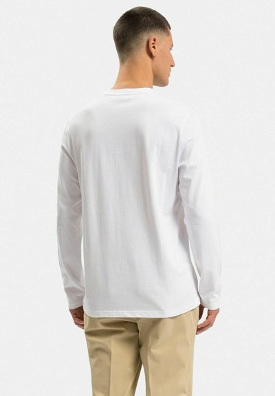 Hvid langærmet t-shirt lavet af bomuld, med rund halsudskæring og en afslappet pasform, båret med lyse bukser.