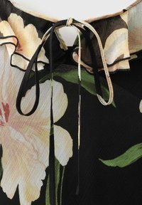 Zwarte blouse met bloemenpatronen in crème, roze en groen. Heeft een gerimpelde halslijn en een vastgebonden koorddetail bij de kraag.