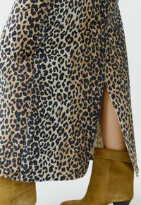 Leopardenmusterrock mit beigem Grund und schwarzen sowie braunen Flecken, seitlichem Schlitzdetail und kombiniert mit kniehohen Wildlederstiefeln.