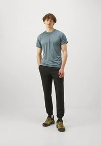 Grå kortermet treningsskjorte kombinert med svarte innsvingte bukser og brune tursko, som viser et avslappet og funksjonelt design.