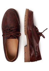 Scarpe in pelle marrone con punta arrotondata e lacci, dotate di suola in gomma tan texturizzata con un motivo a zigzag e dettagli di cucitura minimi.