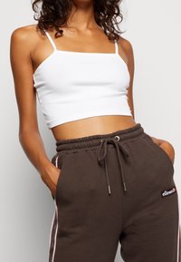 Top corto bianco a costine con spalline sottili abbinato a joggers marroni scuri con vita regolabile e righe rosa sui lati.