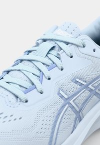 Scarpa da allenamento blu chiaro con tomaia in mesh traspirante, lacci piatti e sottili dettagli viola lungo il lato e intorno ai fori per i lacci.