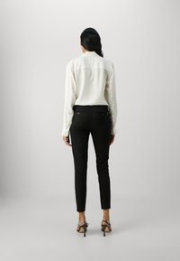 Weiße langärmelige Bluse mit einem geknöpften Kragen, kombiniert mit taillierten schwarzen Hosen und Riemchen-High-Heels. Minimalistisches Design und Texturen.