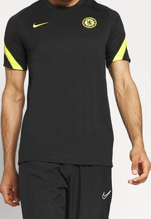 Sort sportstøj med gult Chelsea FC-logo og Nike-swoosh på brystet, gule striber på ærmerne, kombineret med sorte Nike-shorts.