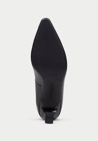 Zapato de tacón negro con punta afilada, parte superior de cuero liso y suela de goma texturizada. Presenta el logo y detalles de tamaño en la suela.