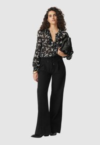 Black floral blouse with long, puffed sleeves and a v-neck, paired with high-waisted wide-leg black trousers and a black clutch bag.