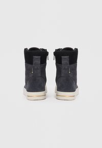 Dunkelgraue Wildleder-Ankle Boots mit hohem Kragen, seitlichen Reißverschlüssen und weißen Sohlen mit einem goldenen Akzentstreifen. Glatte Textur und minimalistisches Design.