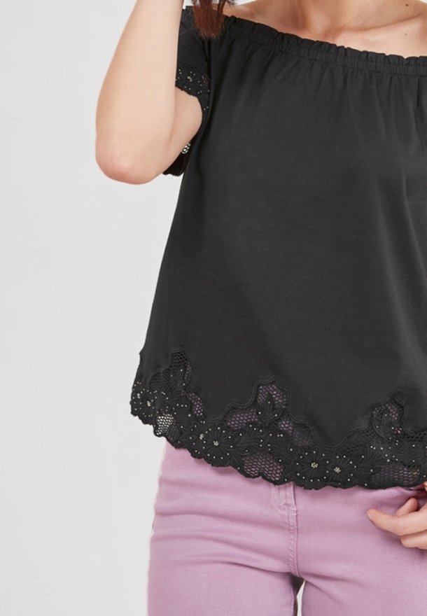 Haut noir décolleté épaules avec une bordure en dentelle texturée à l'ourlet, présentant des bords festonnés et des détails brodés. Associé à un pantalon violet clair.
